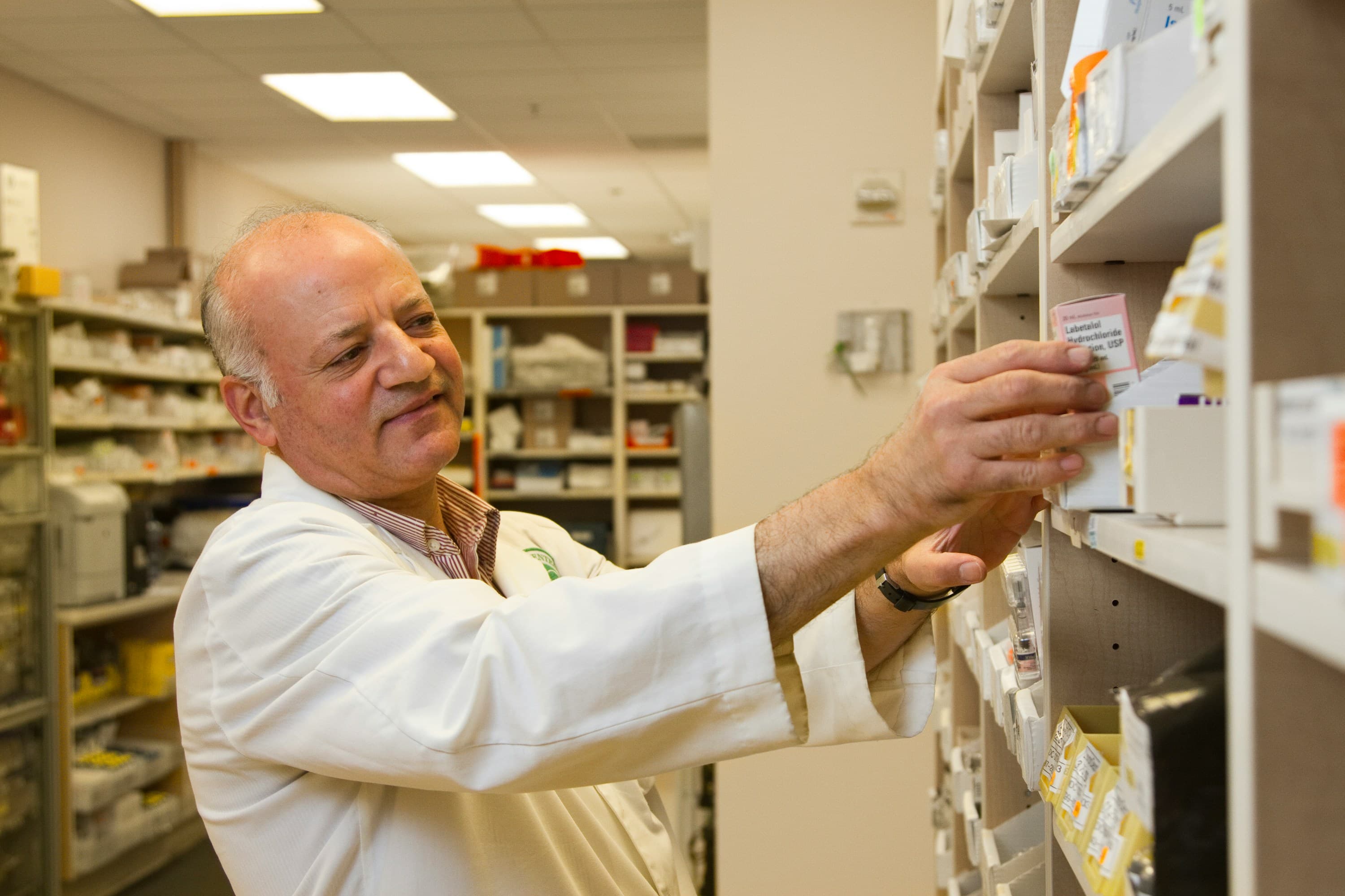 A pharmacist in a white coat taking a product off a shelf