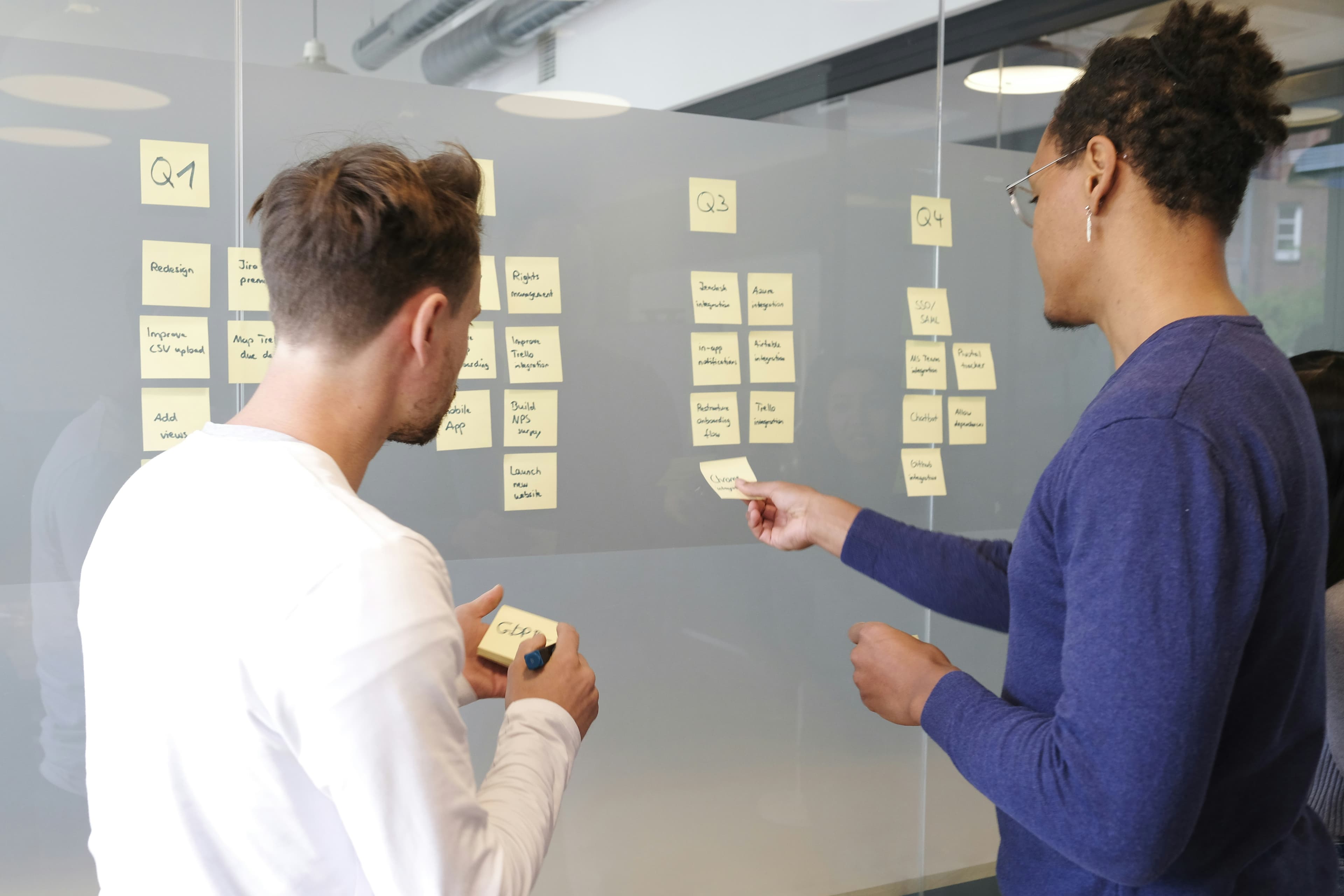 Two people collaborating with sticky notes on glass